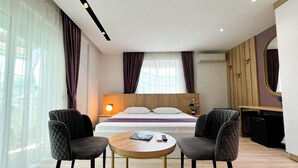 A modern hotel room with a bed, two armchairs, a small round table, and a desk. - Jata Hotel (Tirana)