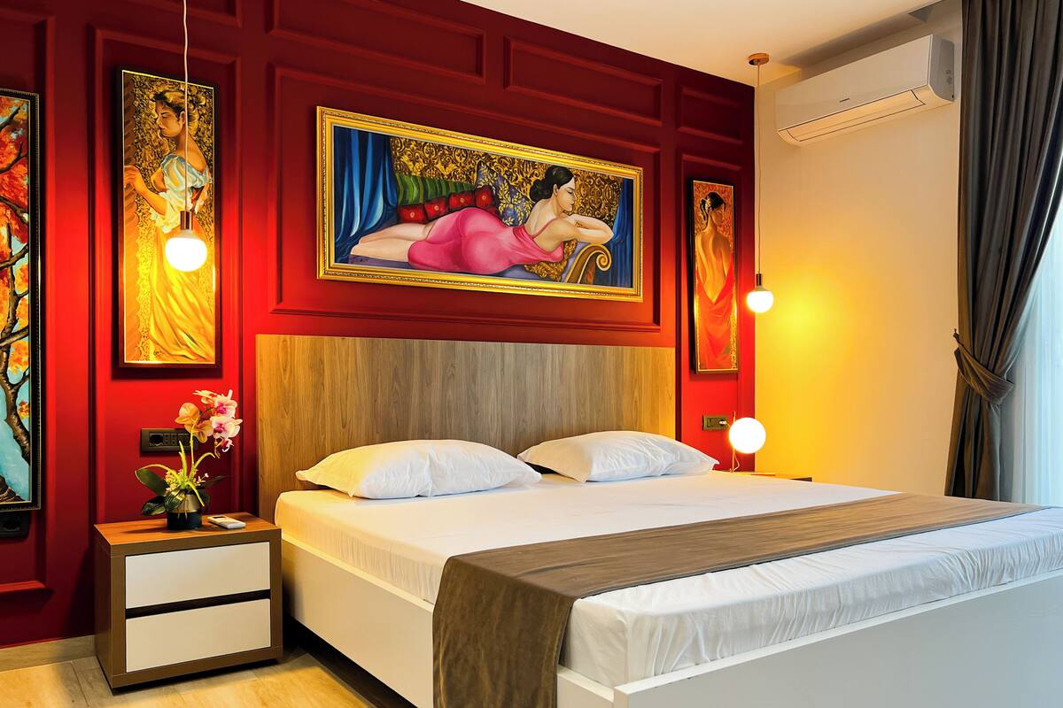 Een hotelkamer met een houten hoofdbord, een bed met witte lakens, een nachtkastje met een bloevas en twee wandlampen.