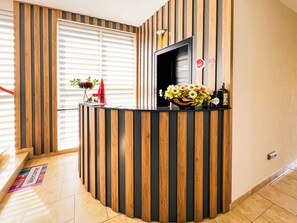 Balcão de recepção com acabamento em madeira, um vaso de flores, uma garrafa e um sinal com uma bandeira vermelha.