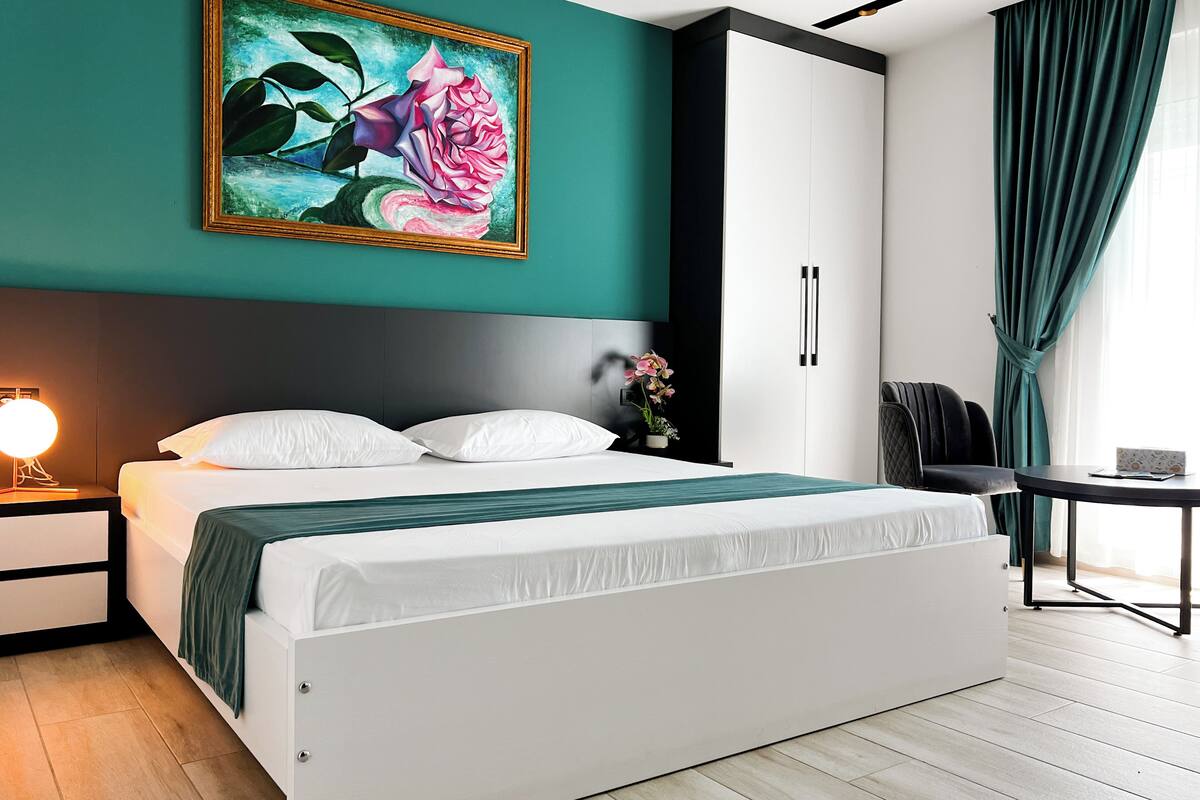 Een moderne slaapkamer met een groot bed, een nachtkastje met een lamp, een bureau en een groen gordijn.