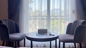 A room with two chairs around a small round table, a window with sheer curtains, and a view of greenery outside. - Jata Hotel (Tirana)