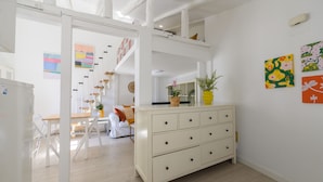Un espacio habitable amplio y luminoso con un aparador blanco, una mesa de comedor y una escalera que sube a un nivel superior.