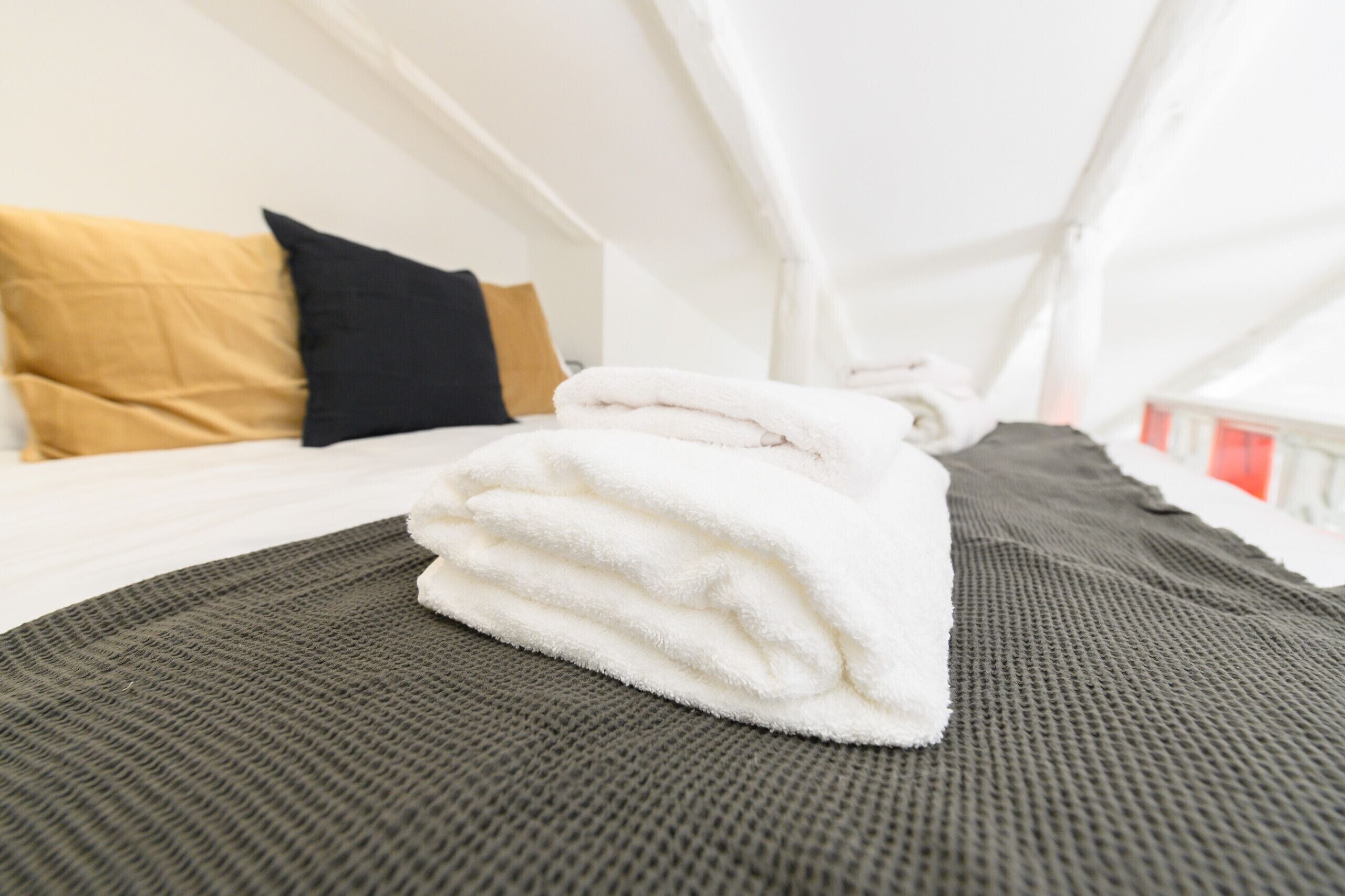 A neatly made bed with white towels, a dark grey blanket, and a black pillow.
