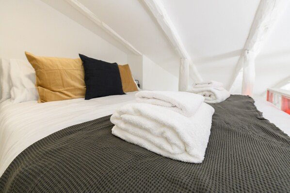 A neatly made bed with white and black pillows, a folded white towel, and a dark gray blanket.