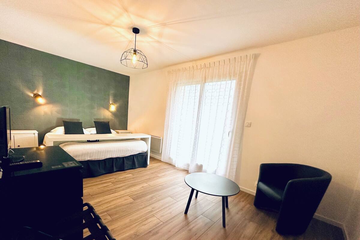 A hotel room with a bed, a desk with a chair, a small table, and a ceiling light fixture.
