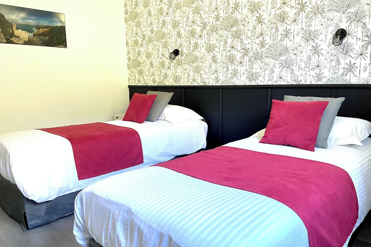 Two single beds with red and white bedding, a black headboard, and a floral wallpaper pattern.