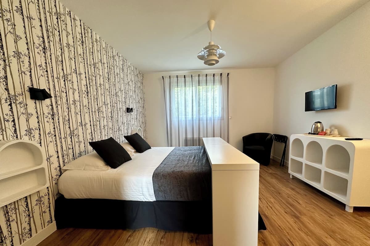 A bedroom with a bed, a desk, a chair, a TV, and a window with curtains.