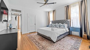 A bedroom with a large bed, a ceiling fan, a nightstand, a lamp, and a window with curtains. - Downtown Elegant Home w/ Grill Near Riverwalk (Columbus)
