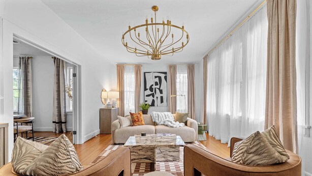 A modern living room with a sofa, coffee table, and two armchairs. There is a chandelier, a large abstract painting, and a dining area in the background. - Downtown Elegant Home w/ Grill Near Riverwalk (Columbus)