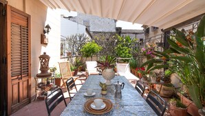 Un espace extérieur abrité, aménagé pour les repas, avec une table carrelée, des chaises, des plantes en pot et une porte en bois rustique.