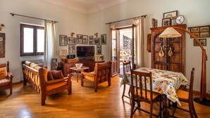 Un salon spacieux, meublé en bois, avec un téléviseur et un coin repas agrémenté d’une nappe à motifs floraux.