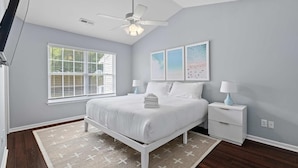 A bedroom with a bed, a nightstand, a ceiling fan, a window with blinds, and artwork on the wall.