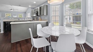 A modern kitchen with a central island, white chairs, and a round marble table.