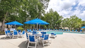 A poolside area with blue umbrellas, white lounge chairs, and a sign indicating no lifeguard on duty.