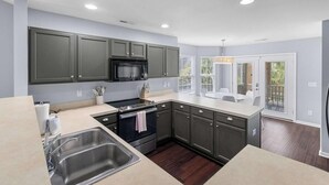 A modern kitchen with dark cabinets, stainless steel appliances, and a large window providing natural light.