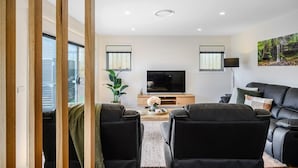Uma sala de estar moderna com televisão de tela plana, sofás de couro preto, mesa de centro de madeira e uma janela grande.