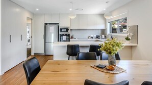 Uma cozinha moderna com armários brancos, uma ilha central e um espaço de refeições com mesa de madeira e cadeiras pretas.