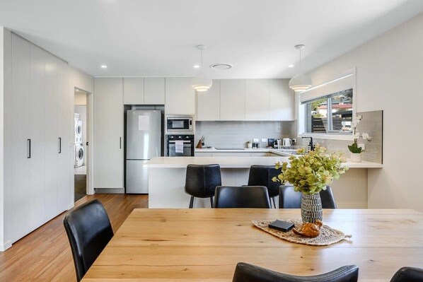 A modern kitchen with white cabinets, a central island, and a dining area with a wooden table and black chairs.