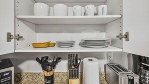 Une cuisine avec des meubles blancs, un plan de travail en granit, un saladier jaune, une pile d’assiettes blanches, un rouleau d’essuie-tout, un grille-pain et un bloc à couteaux.