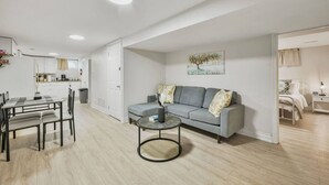 Un salon moderne avec un canapé gris, une table basse ronde et un coin repas comprenant une table et des chaises.