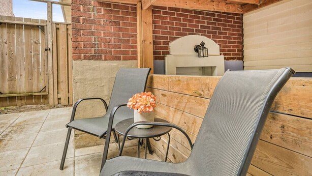 Une terrasse extérieure avec deux chaises en métal et une table, un mur en briques, une clôture en bois et une structure de plafond en bois.