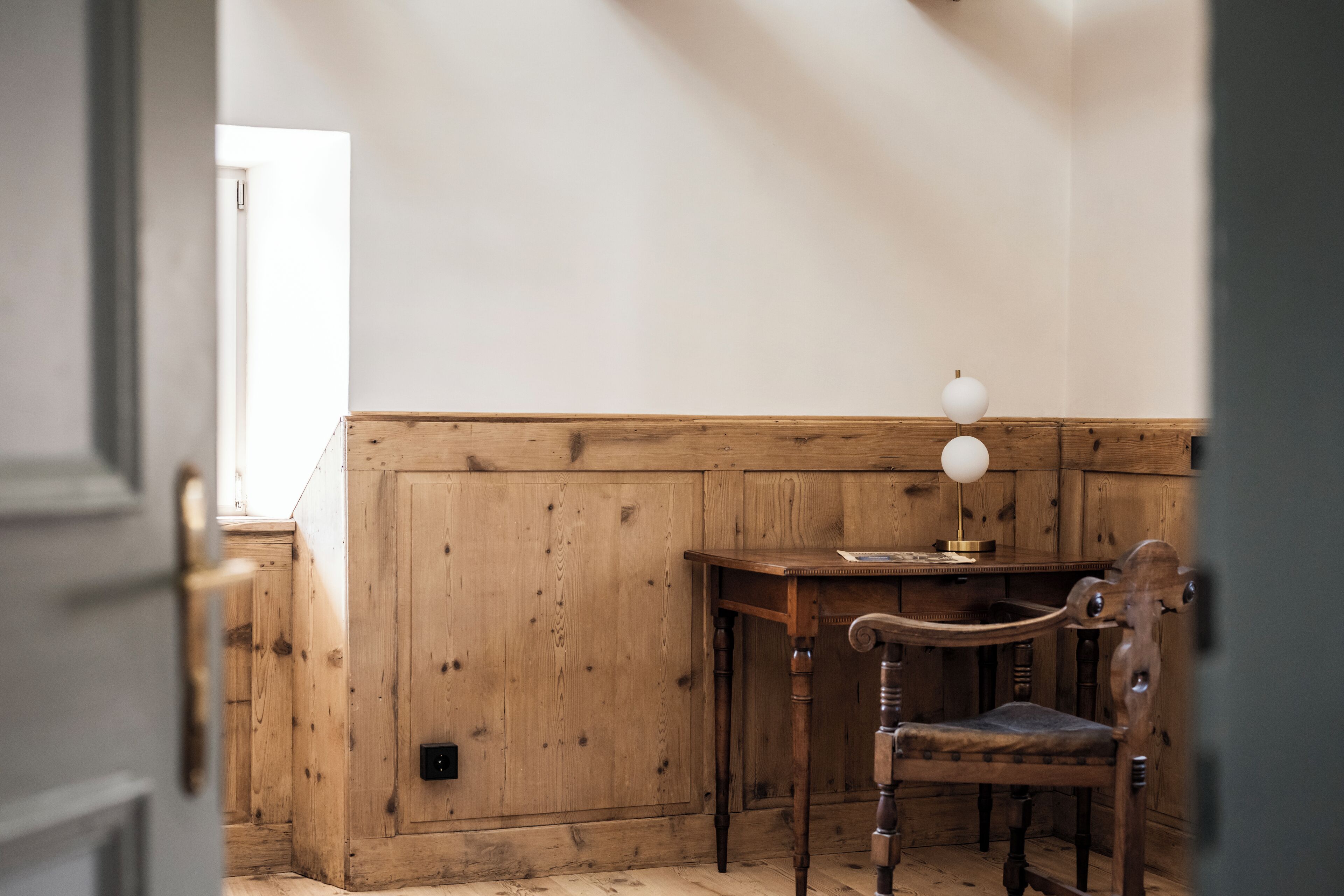 A room with wooden paneling, a desk with a lamp, and a chair.