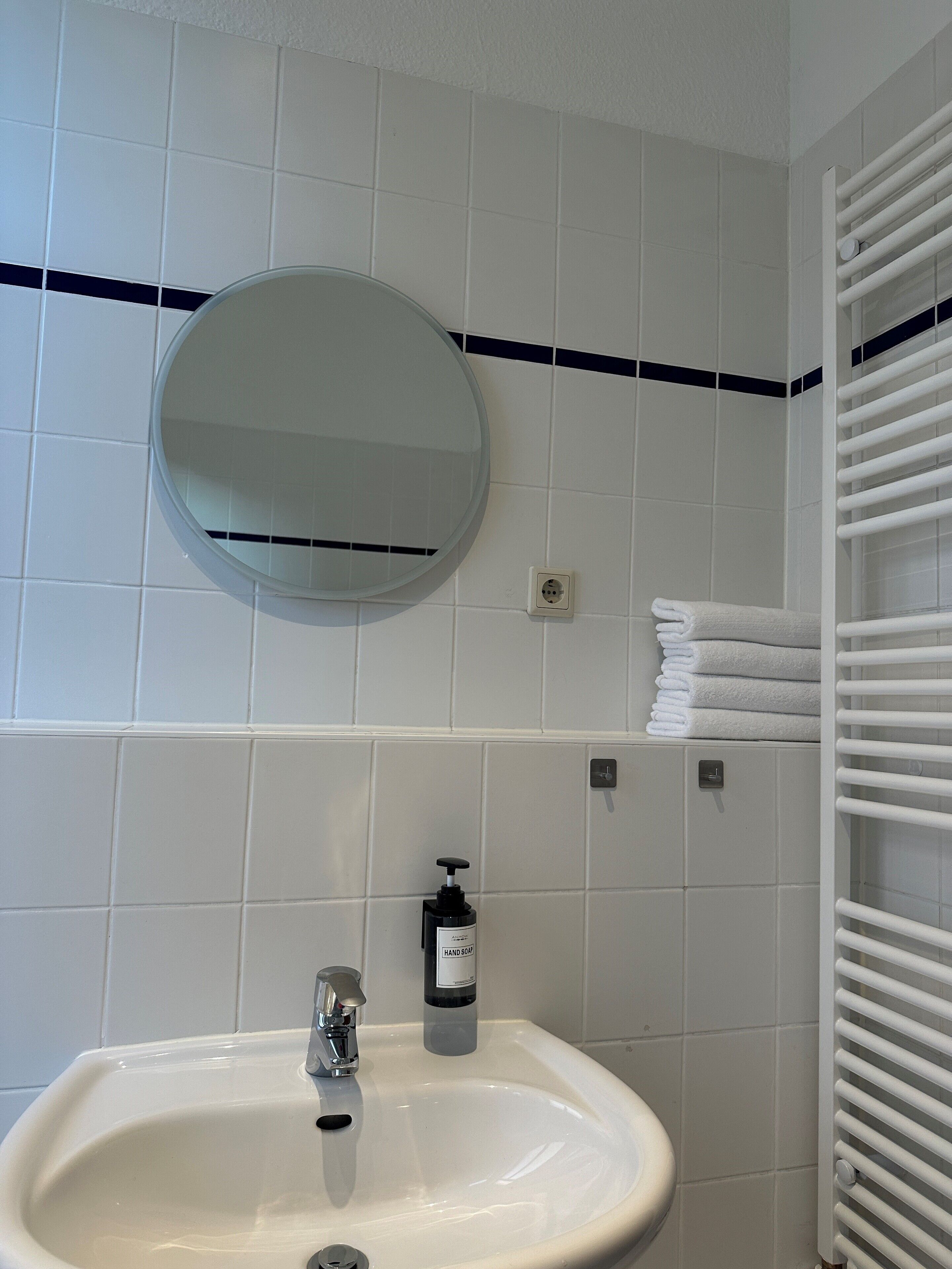 A bathroom with a sink, mirror, towel rack, and hand soap dispenser.