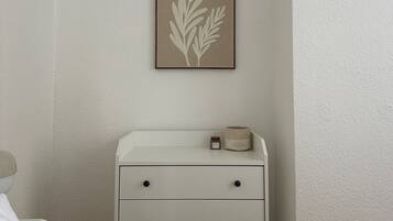 A bedroom with a white dresser, a framed leaf artwork on the wall, and a small jar on the dresser.