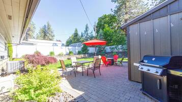 An outdoor patio with a grill, red umbrella, and outdoor furniture.