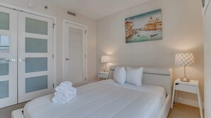 A hotel room with a bed, white curtains, a painting of Venice, and two bedside lamps.