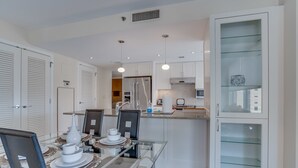 A modern kitchen with white cabinetry, a glass dining table, and a built-in cabinet with glass doors.