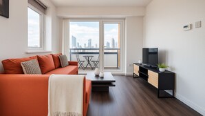 Una sala de estar moderna con sofá, mesa de centro, mueble para televisión y balcón con vista a la ciudad.