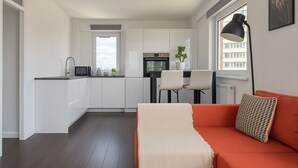 Una cocina moderna con armarios blancos, un comedor con dos sillas y un sofá rojo con una manta.