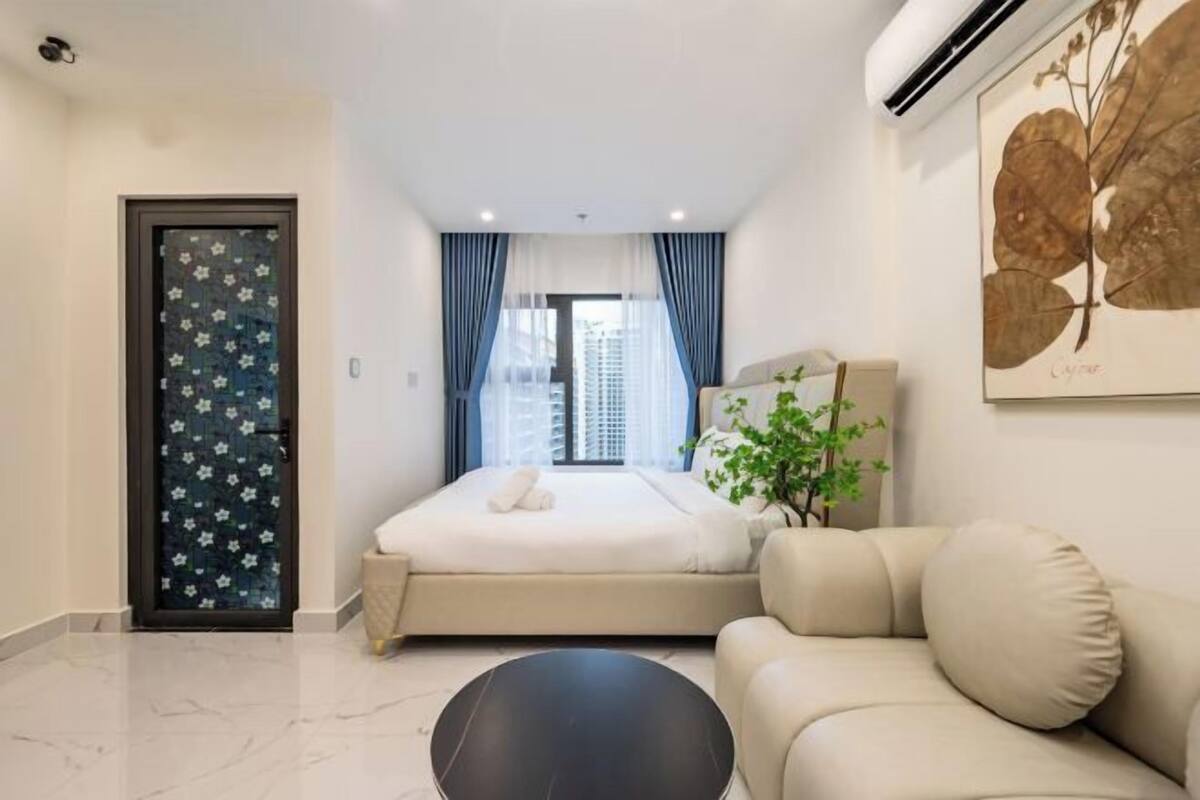 A modern hotel room with a bed, a sofa, a small table, and a window with curtains.