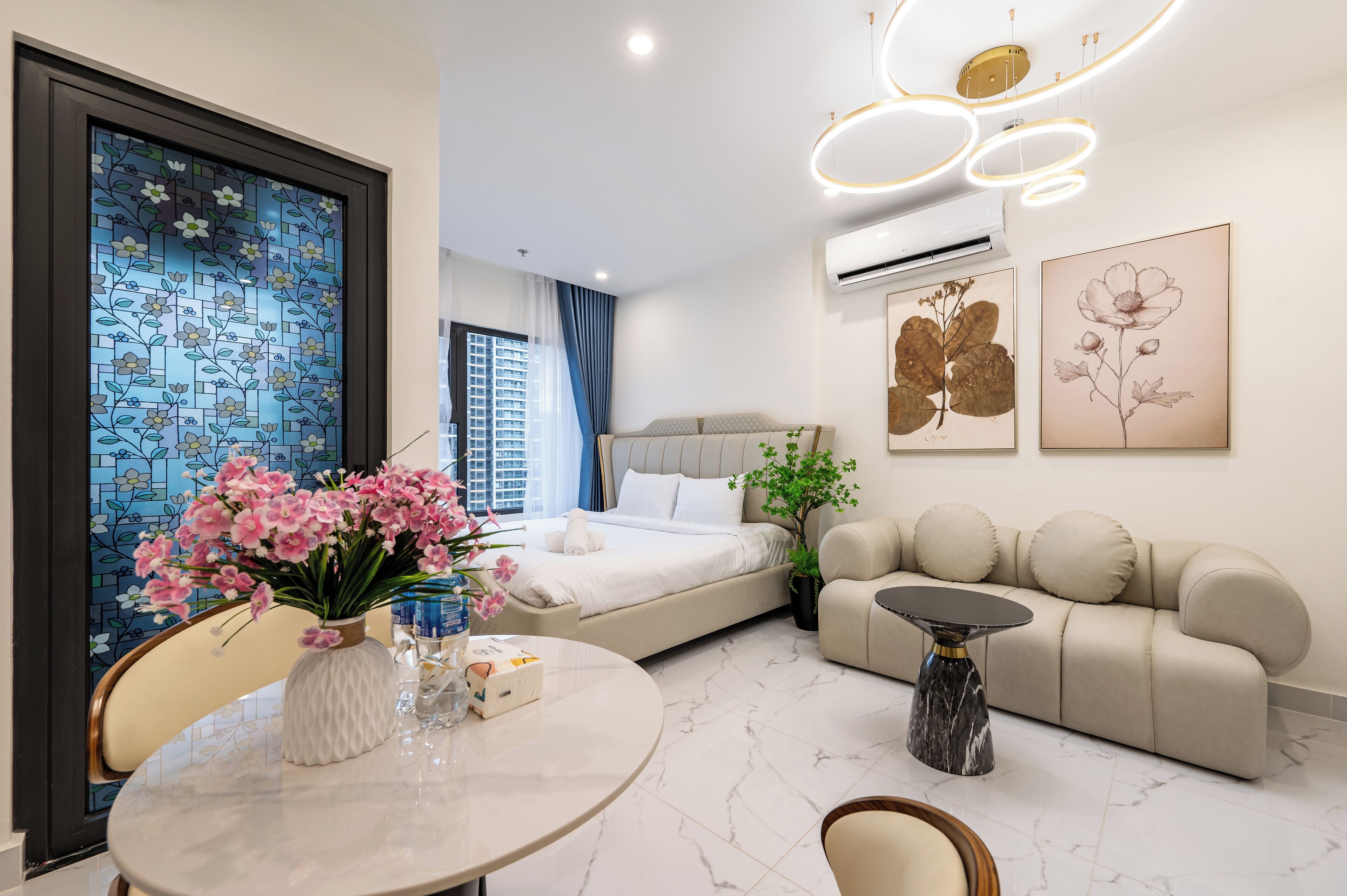 A modern hotel room with a bed, sofa, dining table, and artwork.