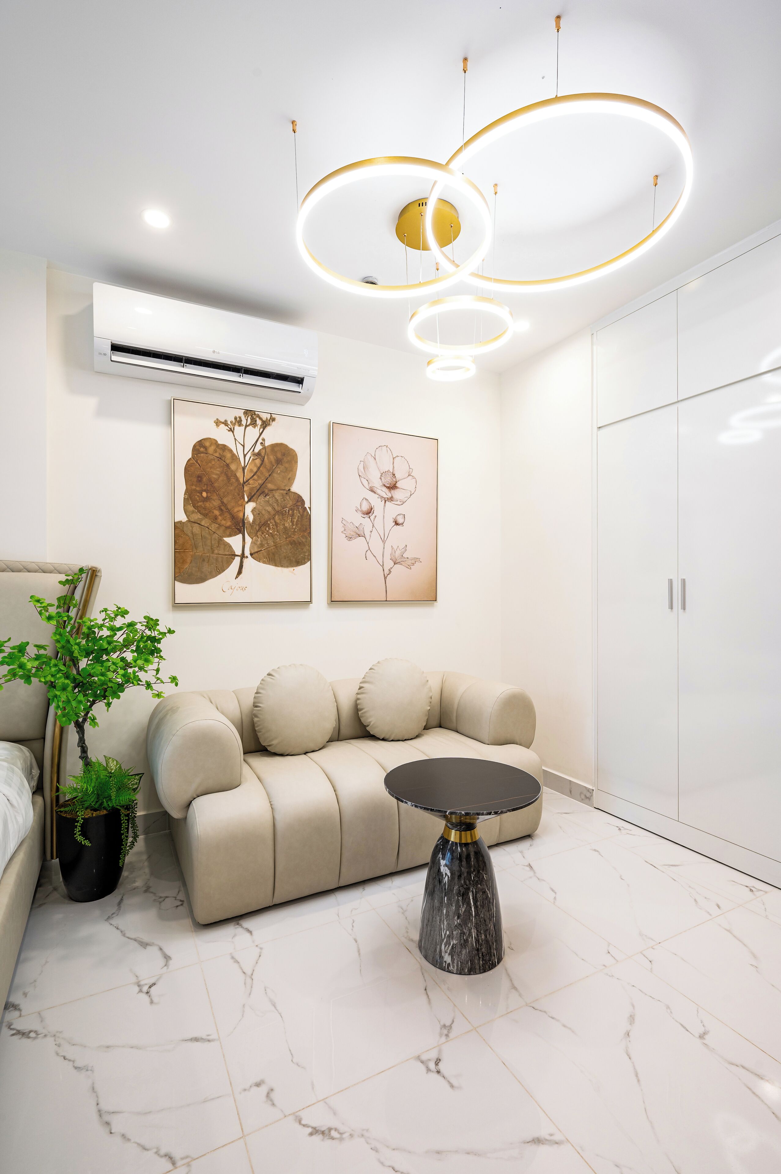 Een moderne woonkamer met een beige bank, een marmeren vloer en een ronde tafel. Er zijn twee wandgemonteerde airconditioners en een plafondlamp.