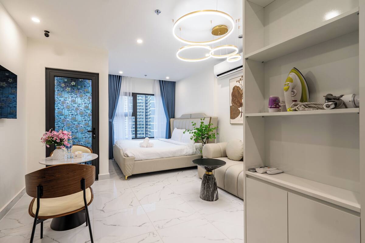 A modern bedroom with a bed, a sofa, a dining table with chairs, and a small side table.