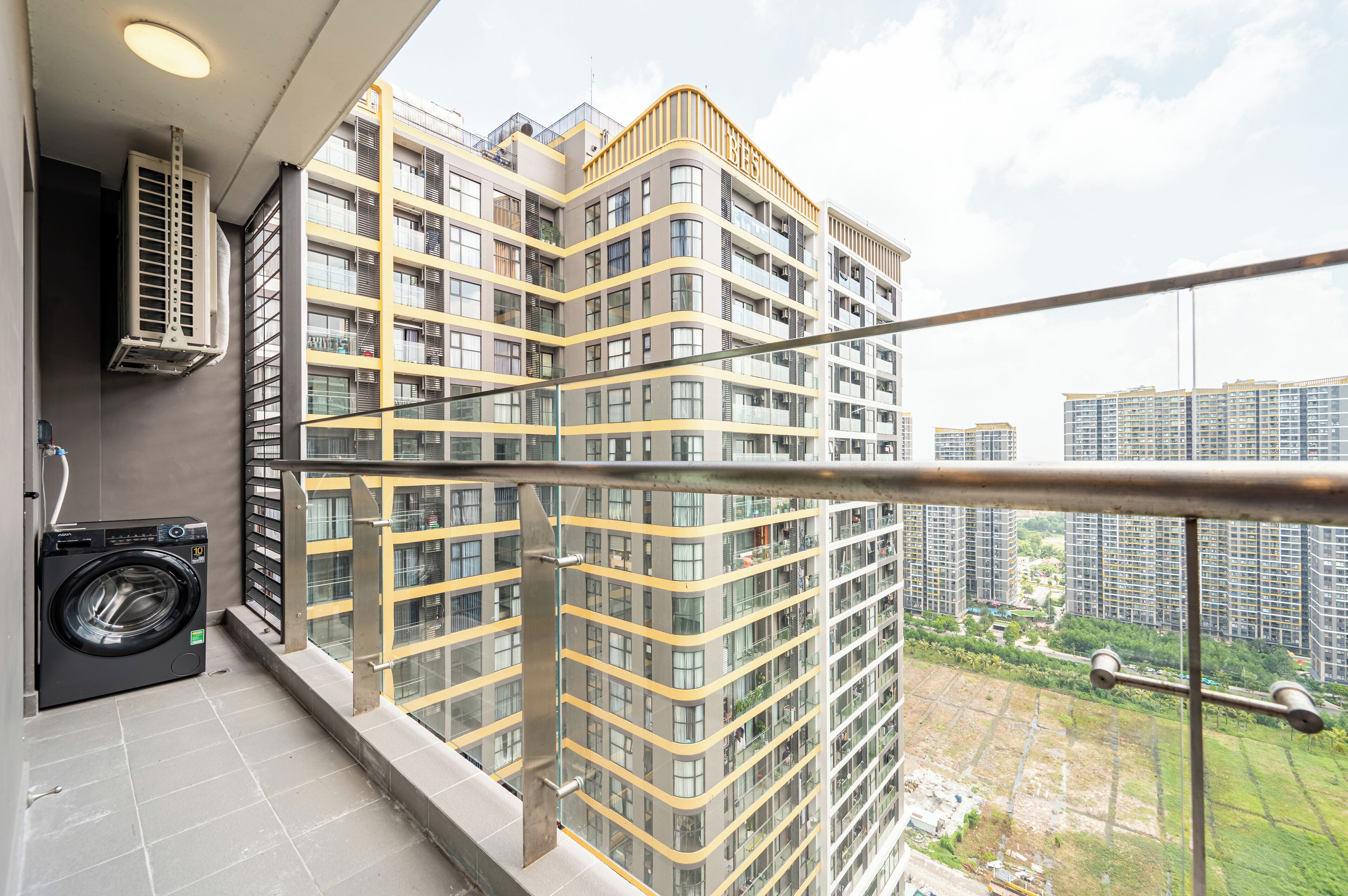 A balcony with a washing machine, air conditioning unit, and a view of high-rise buildings.