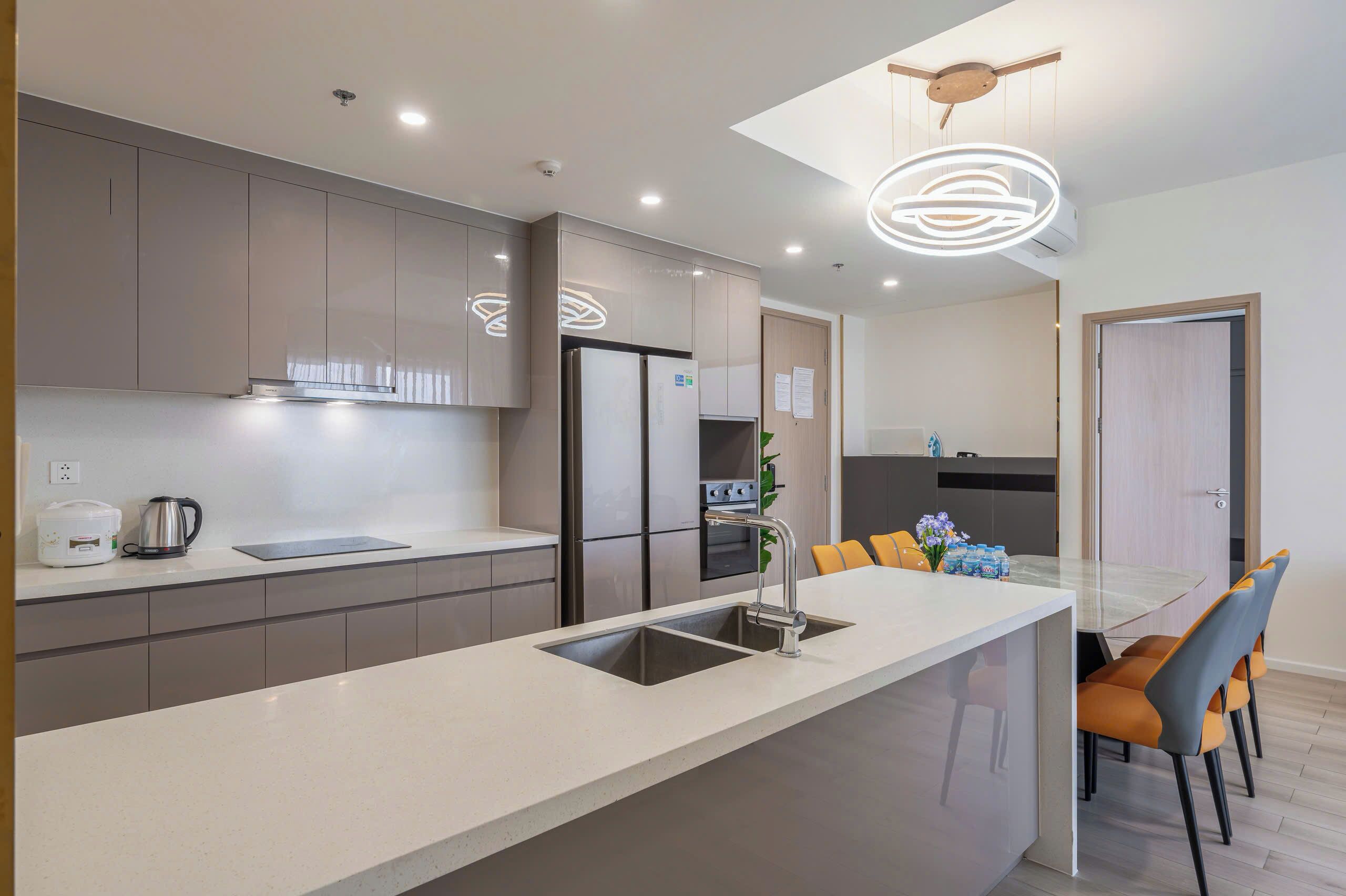 A modern kitchen with a central island, stainless steel appliances, and a dining area with orange chairs.