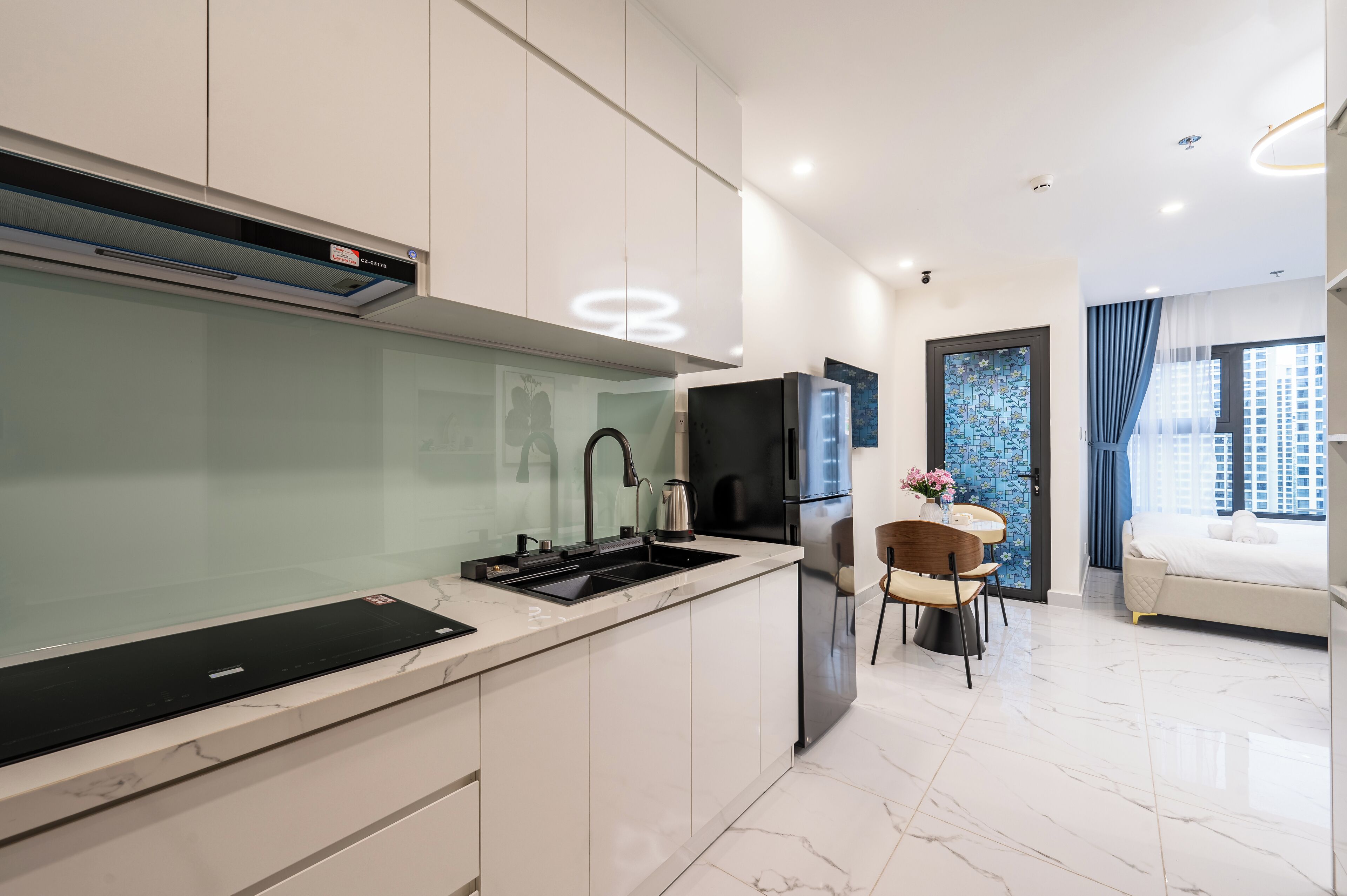A modern kitchen with a built-in stove, a sink, and a refrigerator. There is a dining area with a table and chairs.