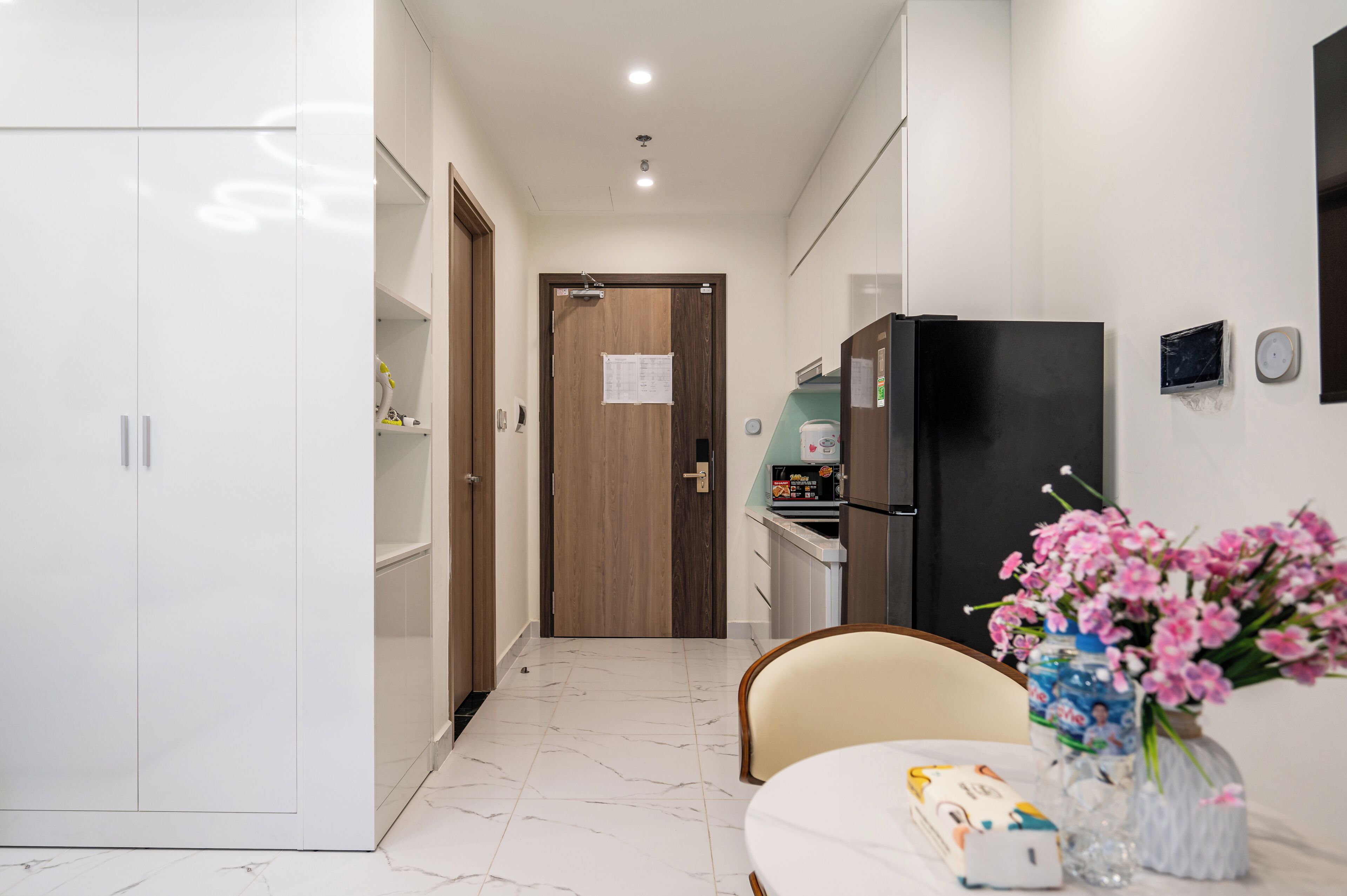 A modern kitchen with a refrigerator, a dining table with a vase of flowers, and a wooden door with a paper on it.