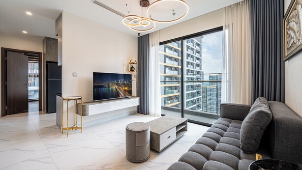A modern living room with a large TV, comfortable seating, and a view of the cityscape through large windows. - Studio - GH5 - Vinhomes Grand Park (Ho Chi Minh City)
