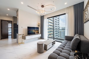 Sala de estar moderna com uma televisão grande, assentos confortáveis e vista para o horizonte urbano através de amplas janelas.