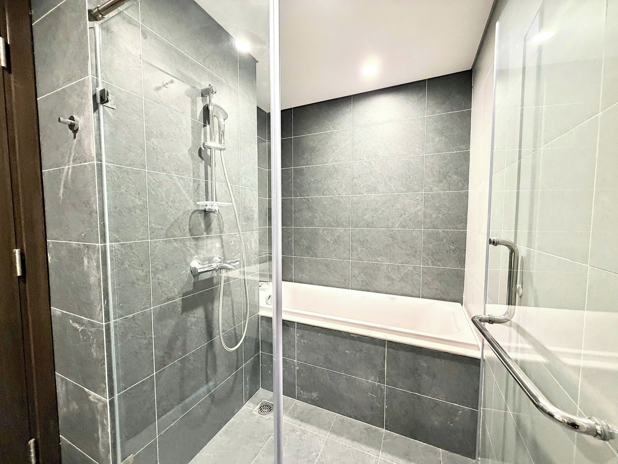 A modern bathroom with a glass-enclosed shower, a separate bathtub, and dark grey tiles.