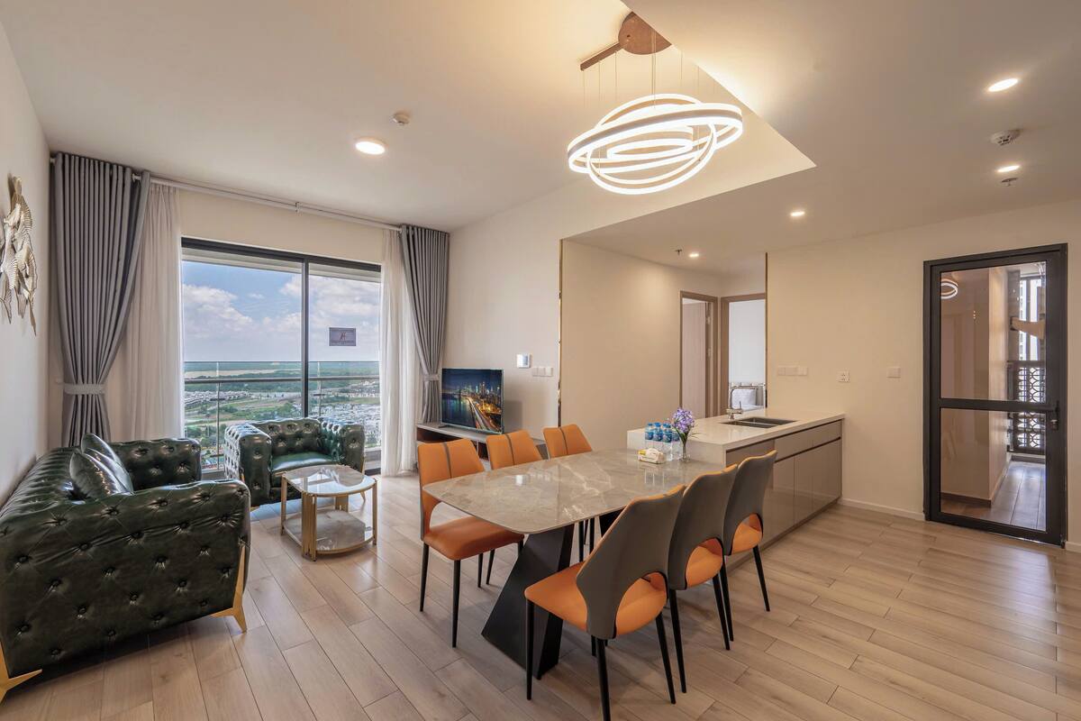 A modern living room with a sofa, dining table, and chairs, a large window with curtains, and a view of the city.
