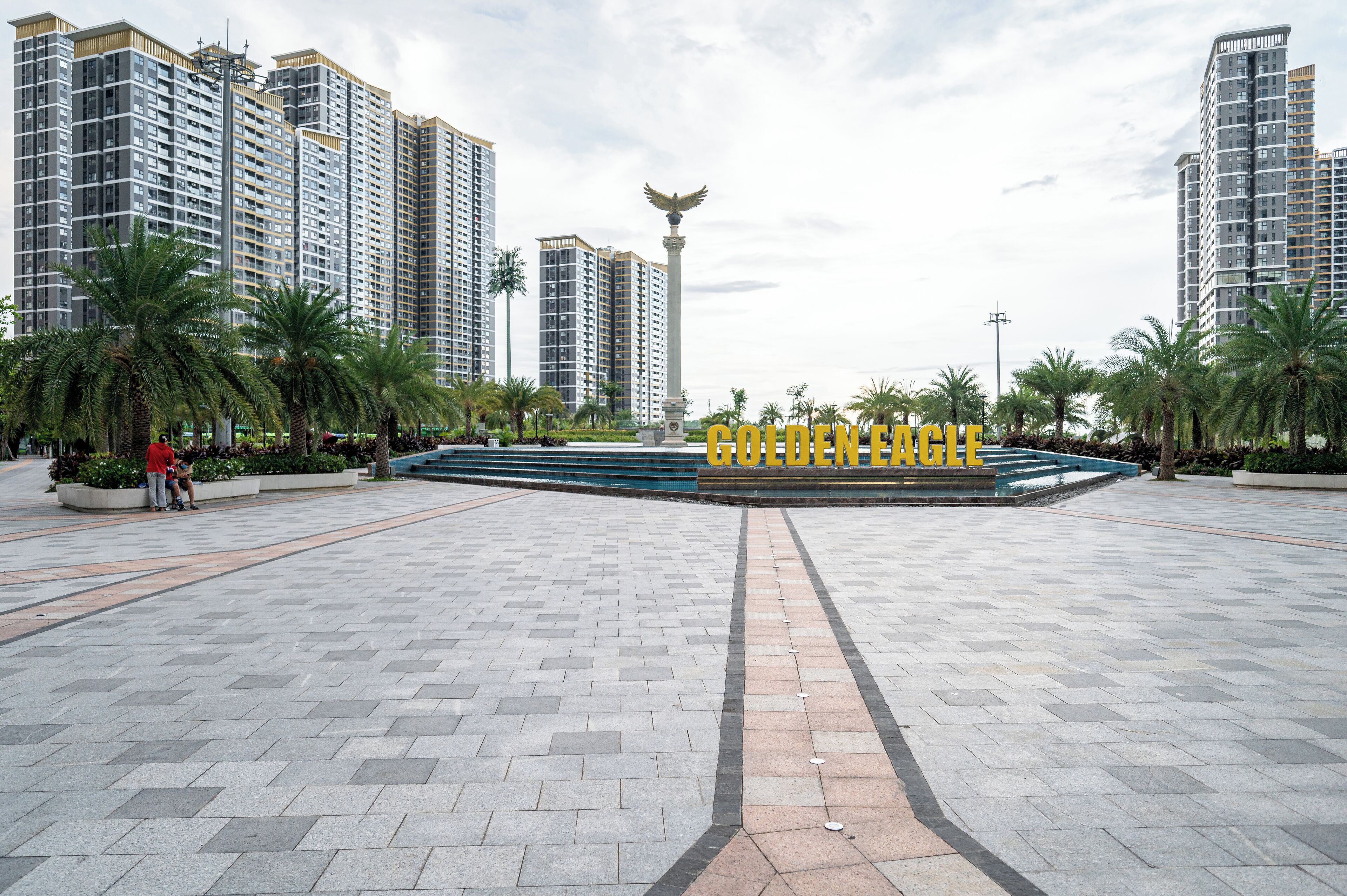 A spacious plaza with a central fountain, surrounded by high-rise buildings and palm trees.