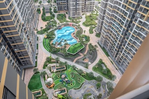 Um edifício residencial alto com piscina central, jardins ajardinados e área de recreação infantil.