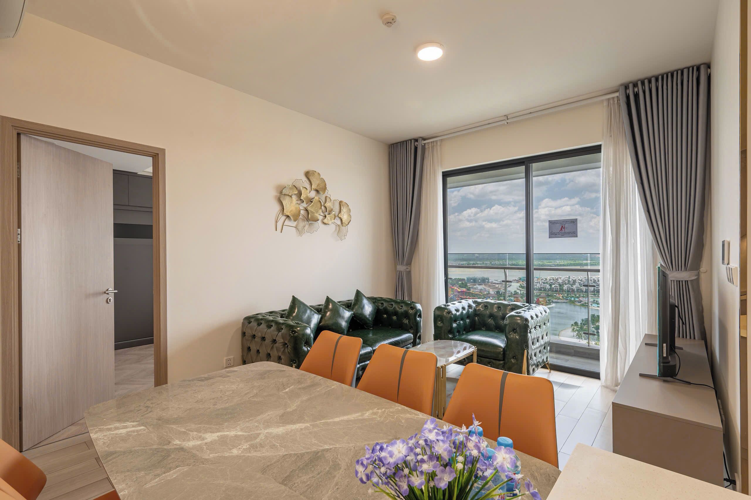 A modern living room with a dining area, a large window with a city view, and a decorative wall piece.