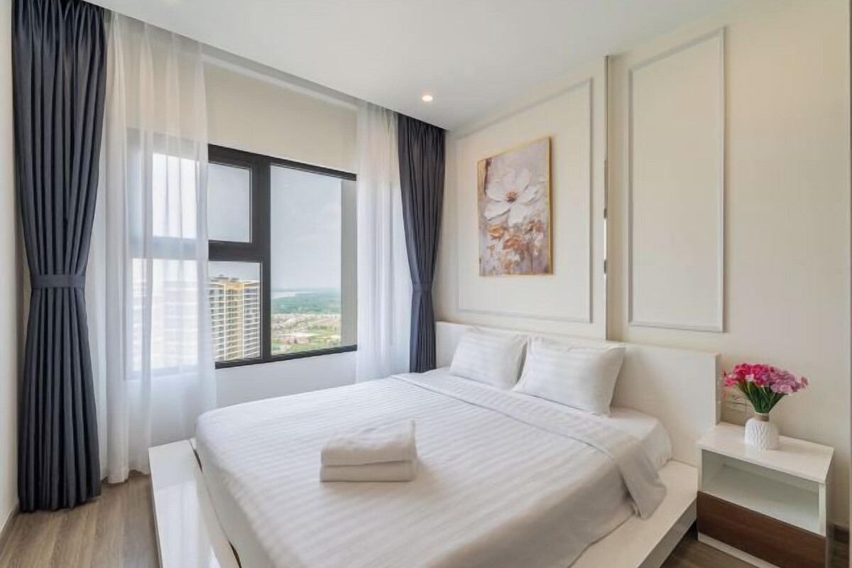 Quarto de hotel moderno com uma cama grande, vista da cidade e um quadro na parede.