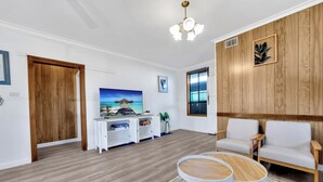 Een moderne woonkamer met houten vloer, witte meubels, een televisie en een groot raam.